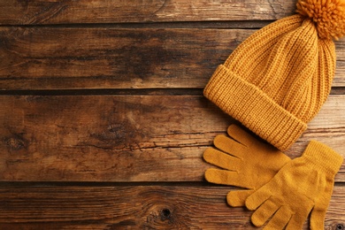 Stylish gloves and hat on wooden background, flat lay. Space for text