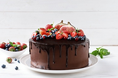 Photo of Fresh delicious homemade chocolate cake with berries on table against wooden background