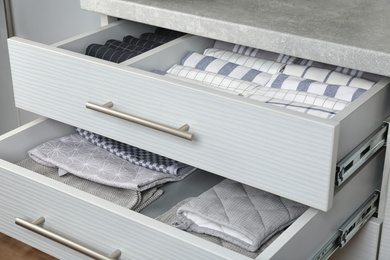 Photo of Open drawers with folded towels and oven mittens. Order in kitchen