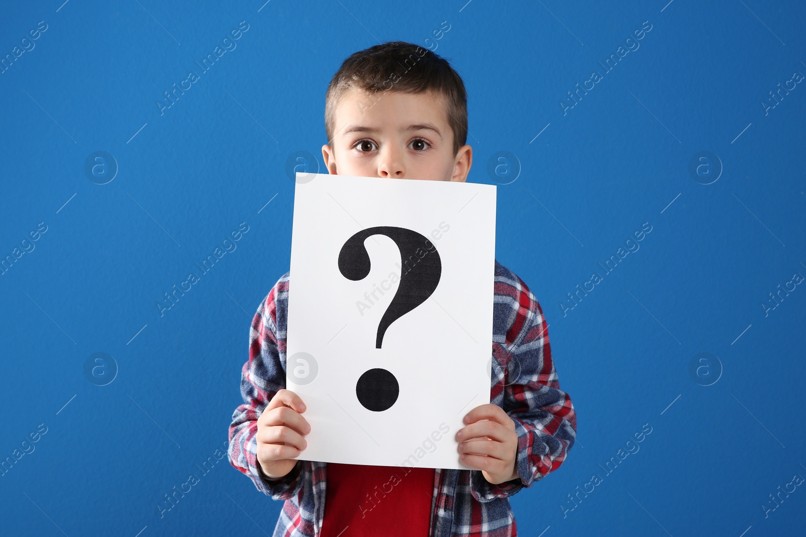 Photo of Emotional little boy holding paper with question mark on blue background