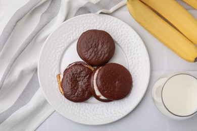 Photo of Tasty sweet choco pies, bananas and glass on milk white table, flat lay