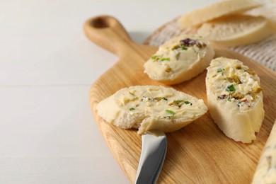 Photo of Tasty butter with olives, green onion, bread and knife on white table, closeup. Space for text