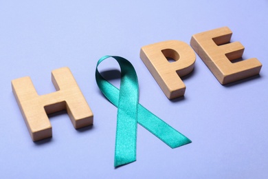 Photo of Word Hope made of wooden letters and teal awareness ribbon on lilac background. Symbol of social and medical issues