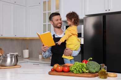 Photo of Cute little girl and her father with recipe book cooking in kitchen