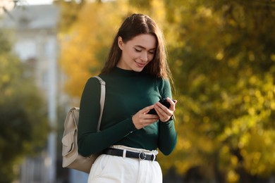 Photo of Young woman with stylish beige backpack and smartphone in park