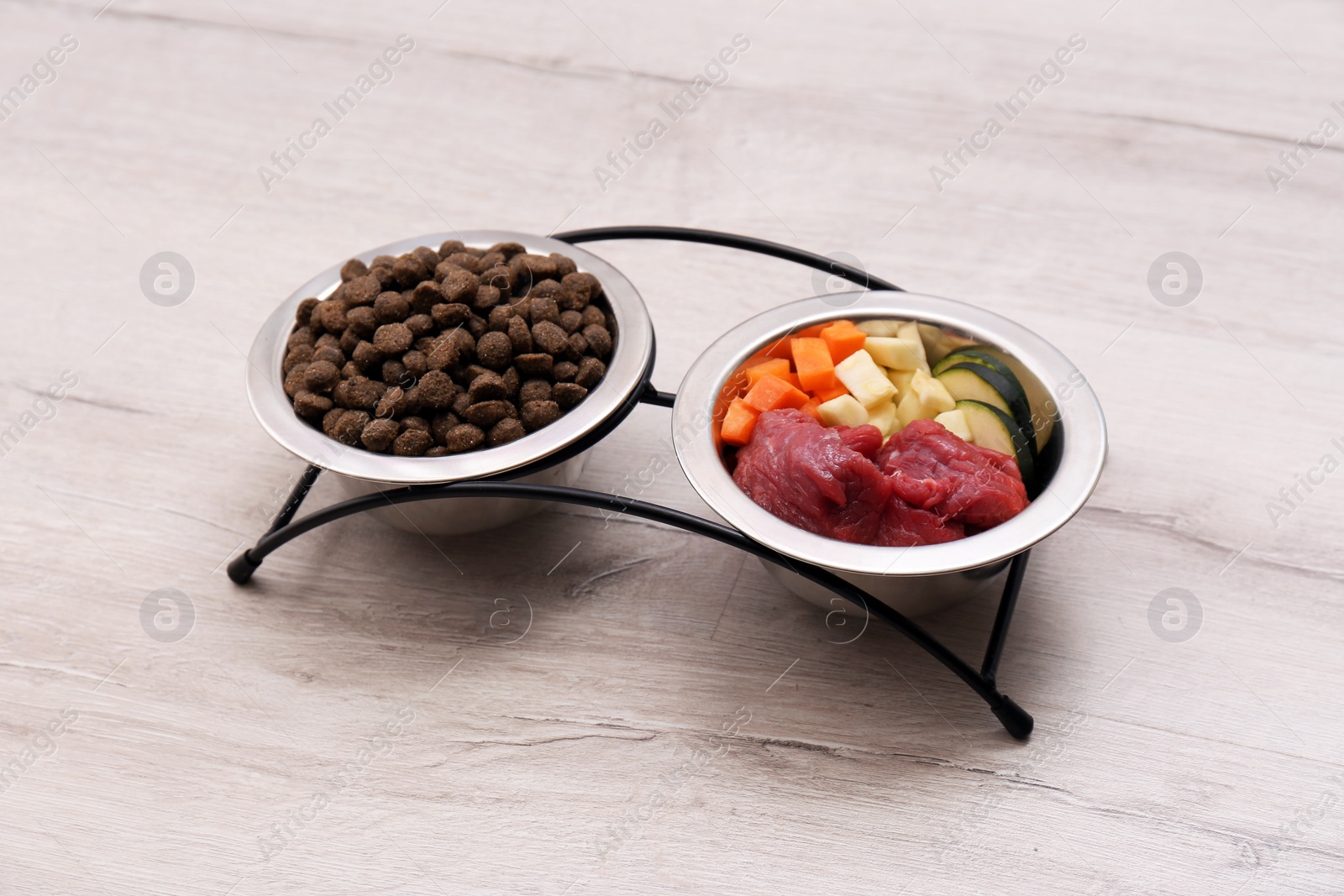 Photo of Bowls with dry and natural dog food on light background