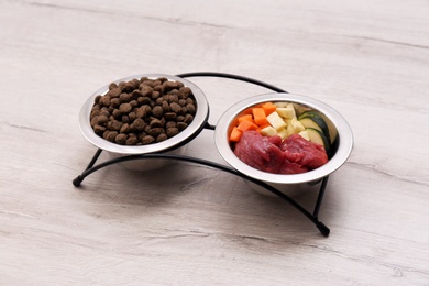 Bowls with dry and natural dog food on light background