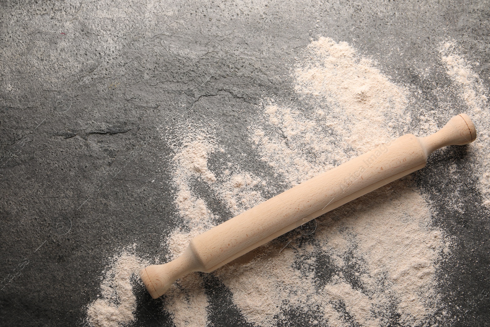 Photo of Scattered flour and rolling pin on grey textured table, top view. Space for text