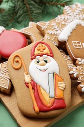 Tasty gingerbread cookies and fir branches on green background, closeup. St. Nicholas Day celebration