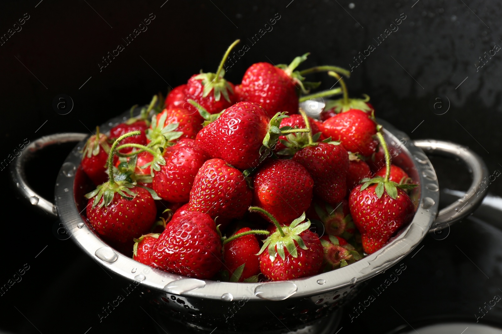 Photo of Metal colander with fresh wet strawberries in sink, closeup