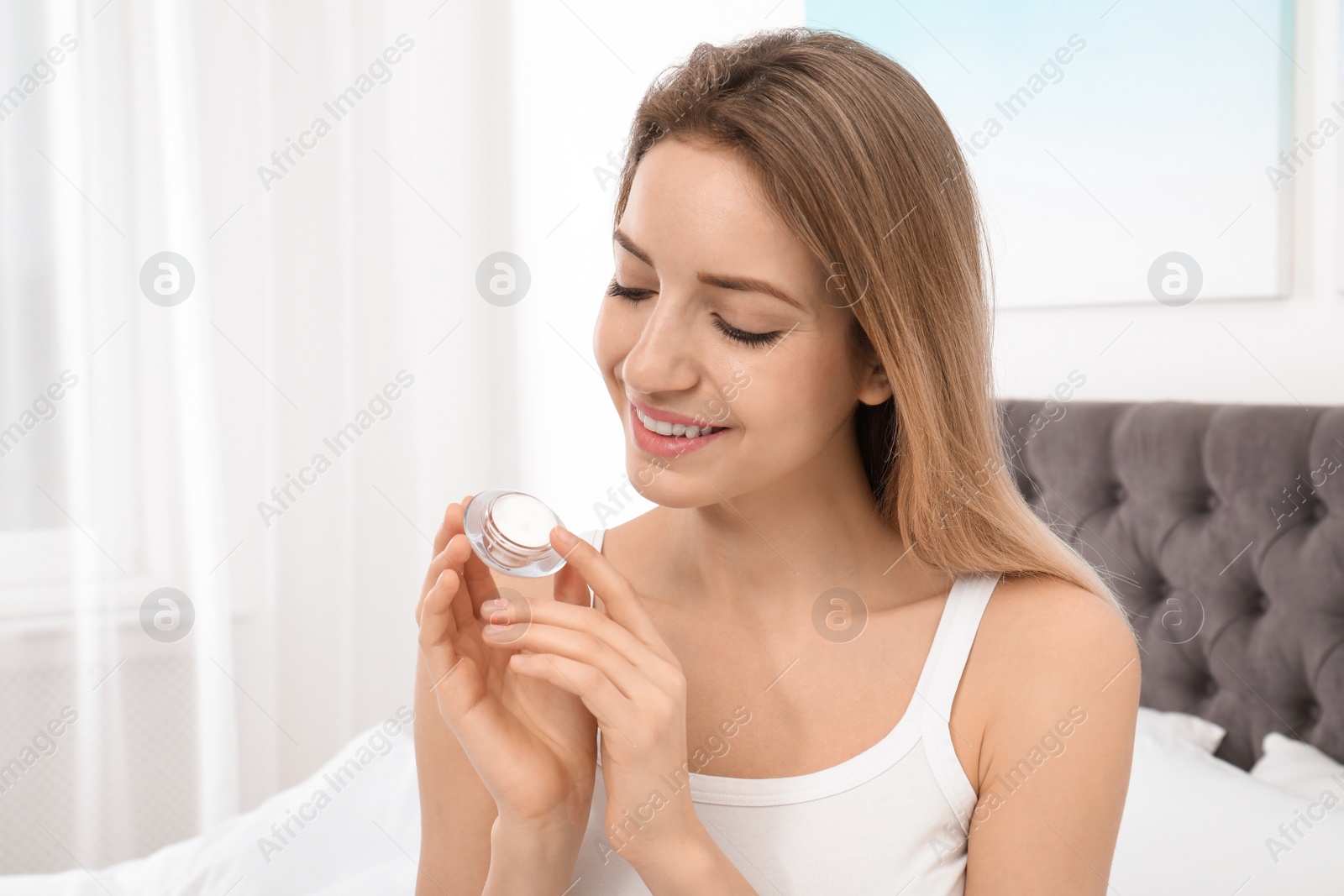 Photo of Portrait of young woman with jar of cream indoors. Beauty and body care