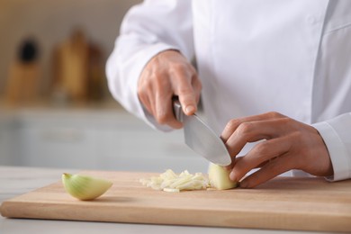 Photo of Professional chef cutting onion at white marble table indoors, closeup