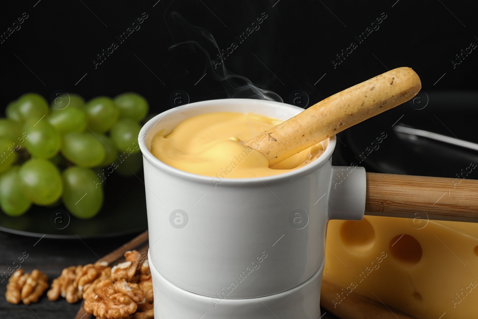 Photo of Pot of tasty cheese fondue and bread stick on black wooden table