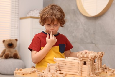 Photo of Cute little boy playing with wooden construction set at table in room. Child's toy