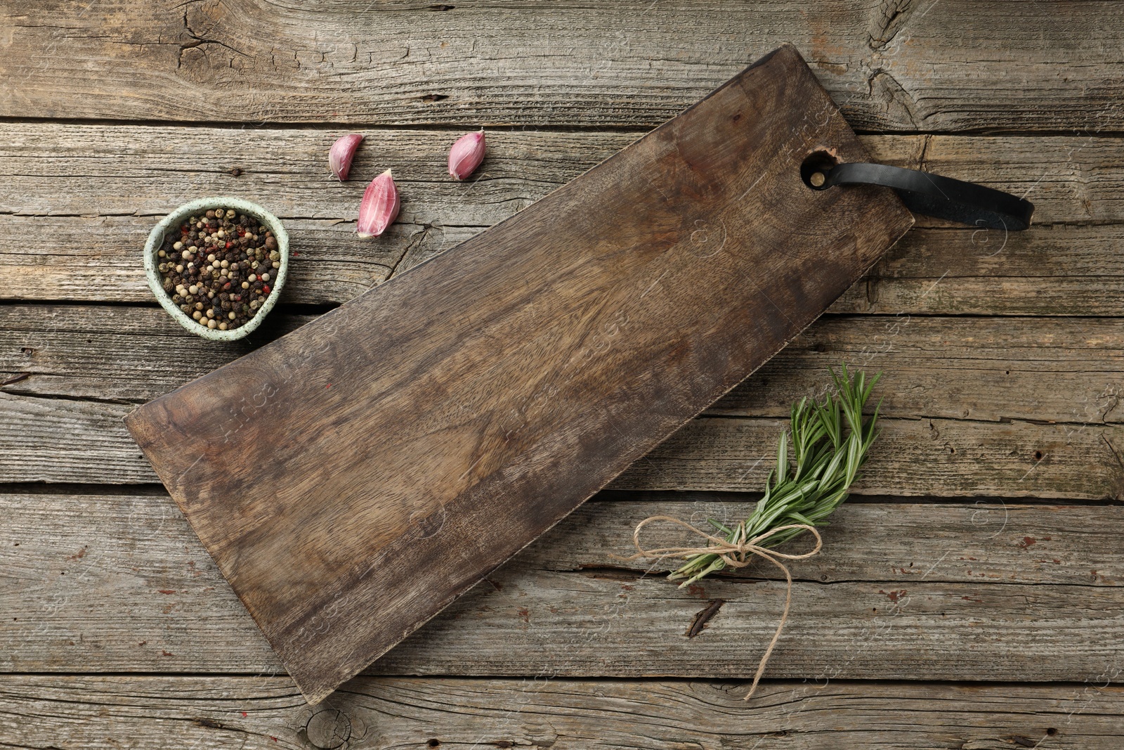 Photo of Cutting board, garlic, pepper and rosemary on wooden table, flat lay. Space for text