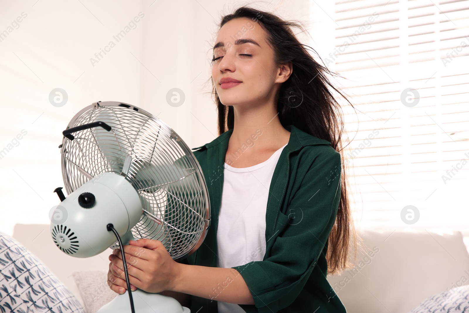 Photo of Woman with fan enjoying air flow at home. Summer heat