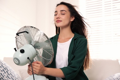 Photo of Woman with fan enjoying air flow at home. Summer heat