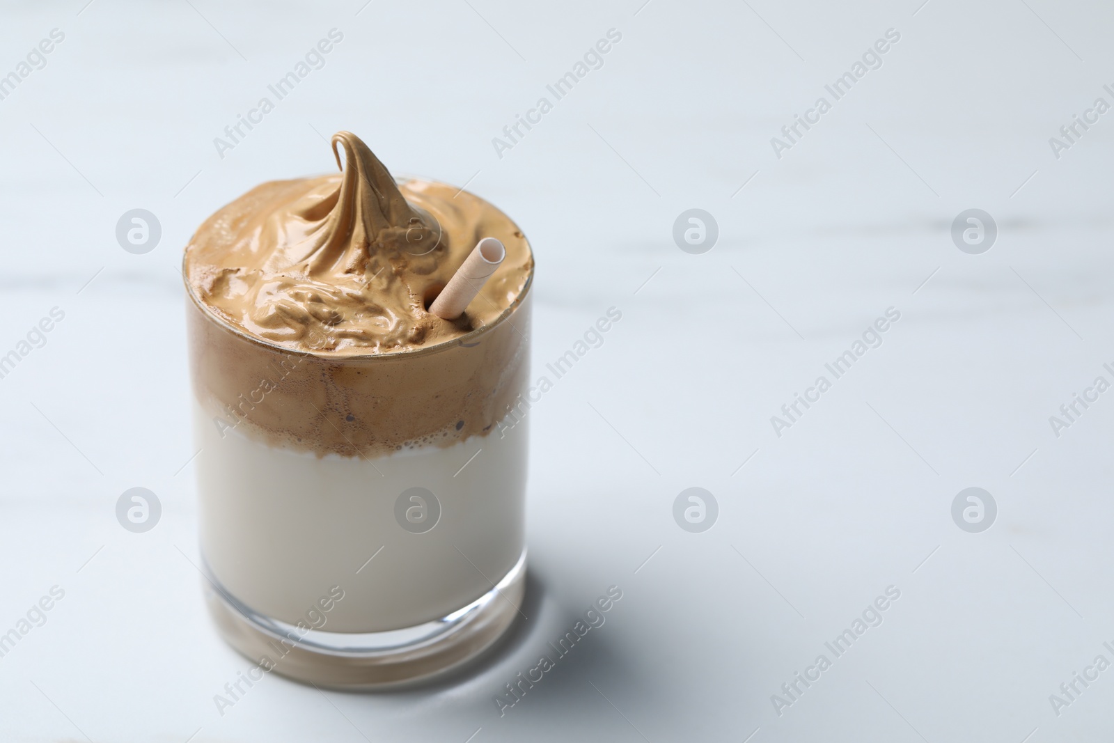 Photo of Glass of delicious dalgona coffee on white marble table, closeup. Space for text