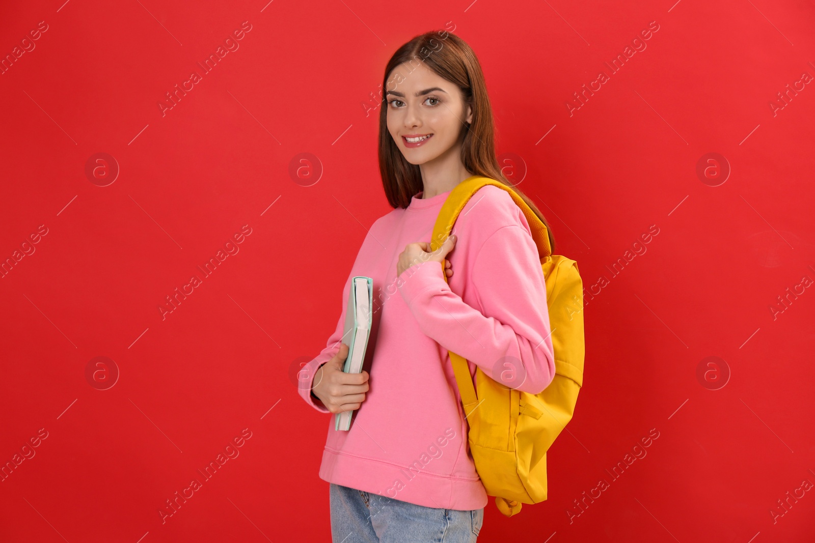 Photo of Teenage student with backpack and book on red background