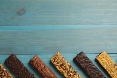 Photo of Different tasty protein bars on light blue wooden table, flat lay. Space for text