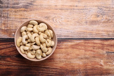 Photo of Tasty cashew nuts in bowl on wooden table, top view. Space for text