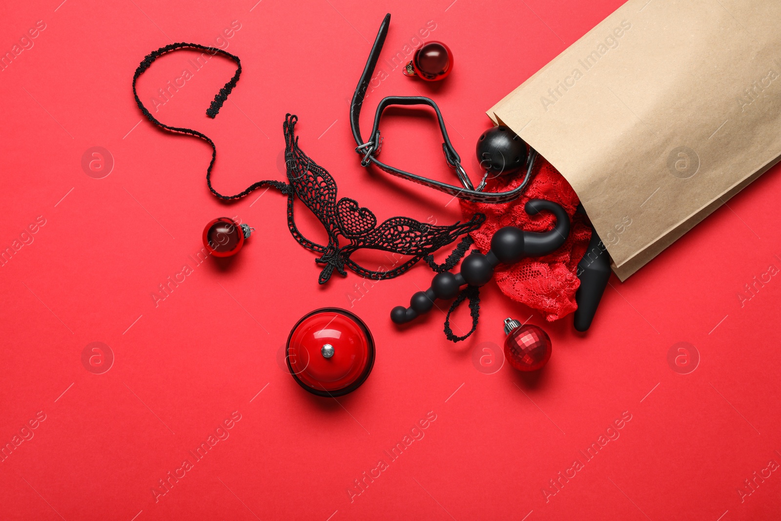 Photo of Paper bag with different sex toys and Christmas balls on red background, flat lay