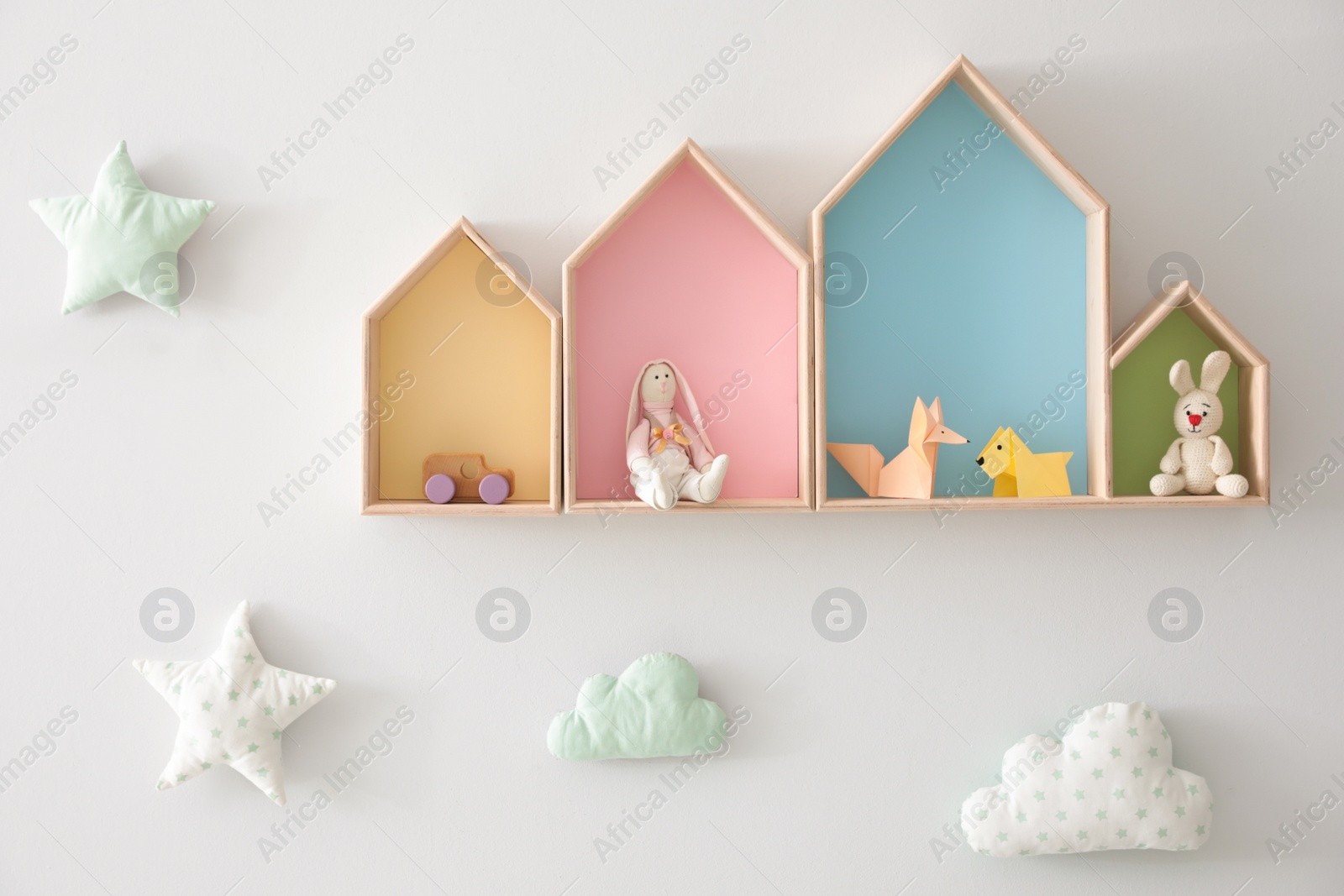 Photo of Different house shaped shelves with toys and decorative clouds on white wall. Interior design