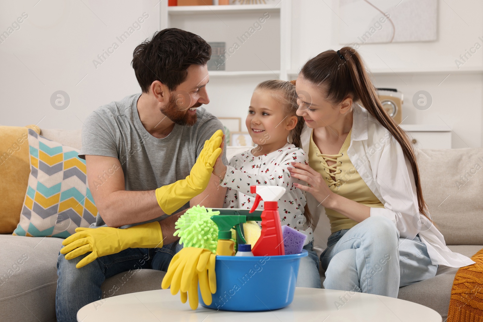 Photo of Spring cleaning. Family with basin of different detergents in living room