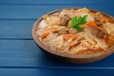 Tasty cabbage soup with meat, carrot and parsley on blue wooden table, closeup. Space for text