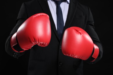 Photo of Businessman in suit wearing boxing gloves on black background, closeup