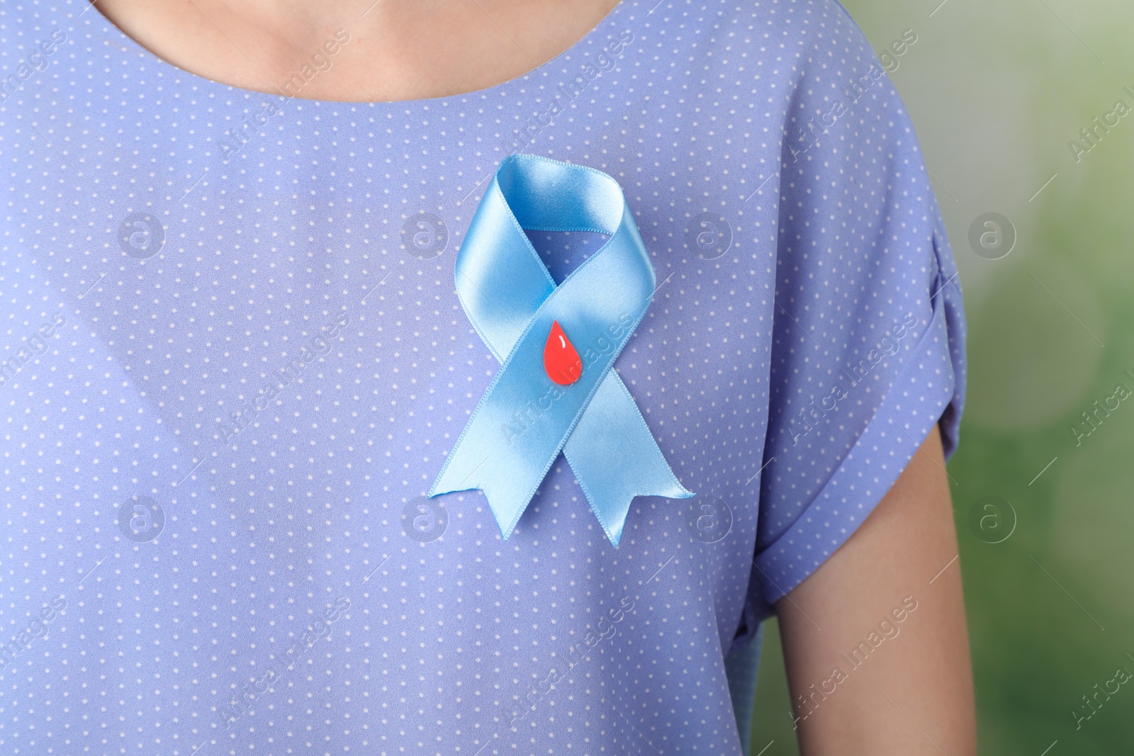 Photo of Woman with light blue ribbon and paper blood drop against blurred green background, closeup. World Diabetes Day