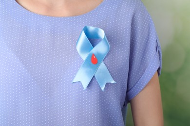Photo of Woman with light blue ribbon and paper blood drop against blurred green background, closeup. World Diabetes Day