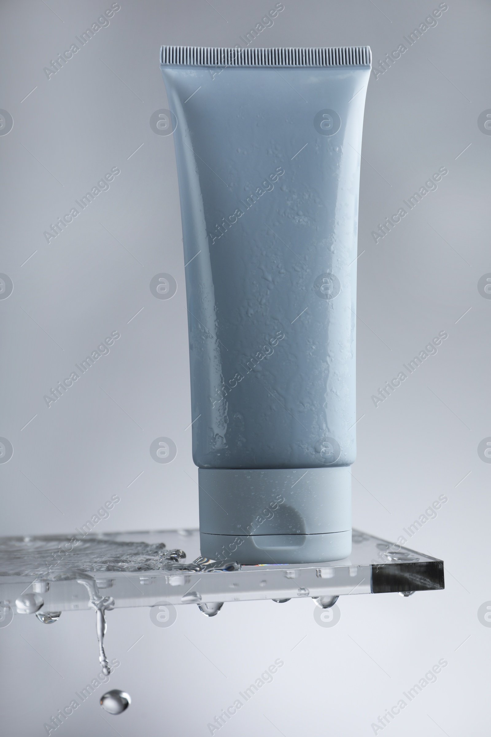 Photo of Moisturizing cream in tube on glass with water drops against grey background