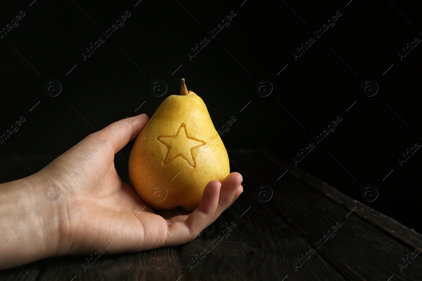 Photo of Woman holding ripe pear with carved star at table against dark background. Space for text