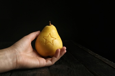 Woman holding ripe pear with carved star at table against dark background. Space for text