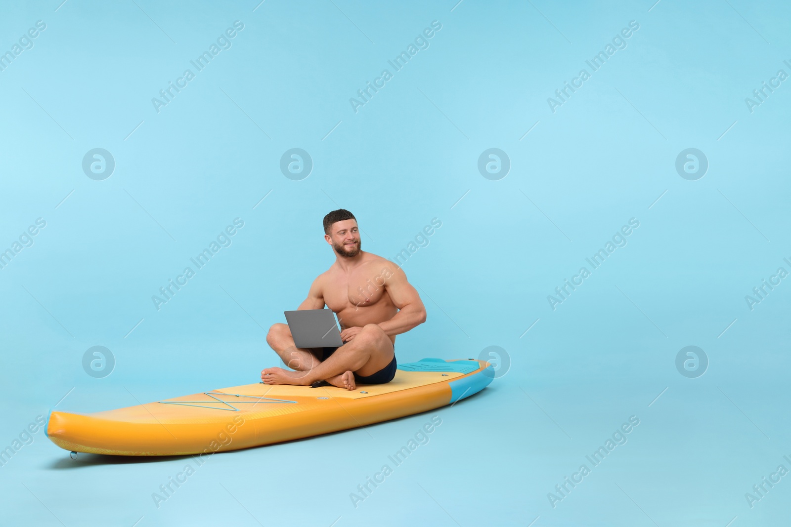 Photo of Man with laptop on SUP board against light blue background