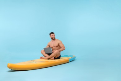 Photo of Man with laptop on SUP board against light blue background