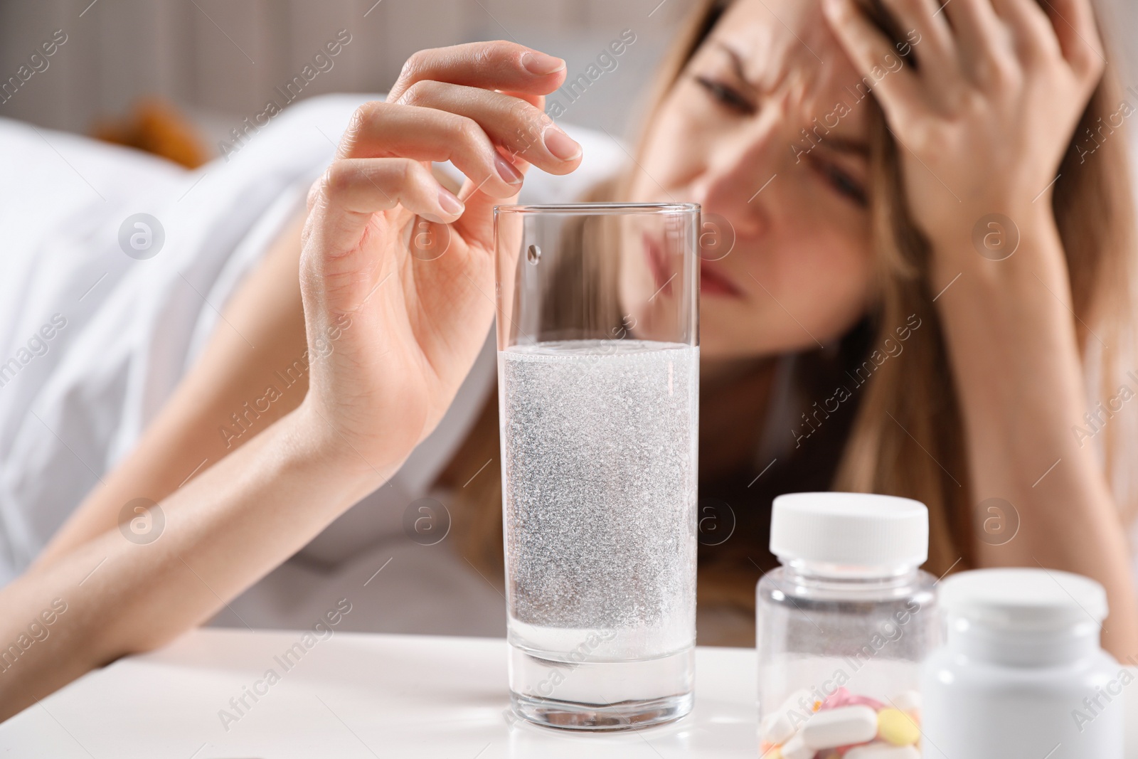 Photo of Woman putting medicine for hangover into glass of water at home, focus on hand with pill