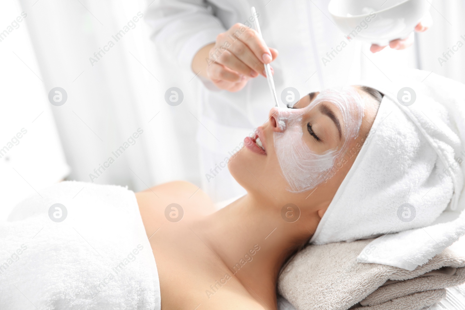 Photo of Cosmetologist applying mask on client's face in spa salon