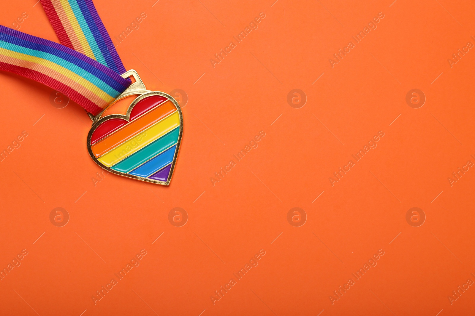 Photo of Rainbow ribbon with heart shaped pendant on orange background, top view and space for text. LGBT pride