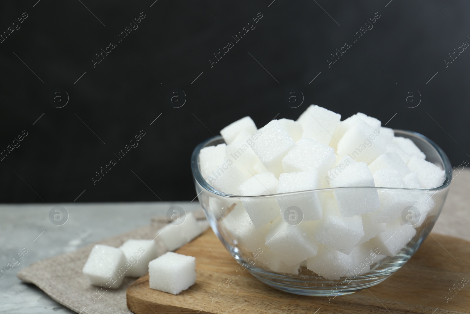 Photo of White sugar cubes in glass bowl on grey table, space for text