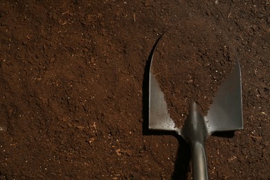 Photo of Metal shovel on fertile soil, top view and space for text. Gardening tool