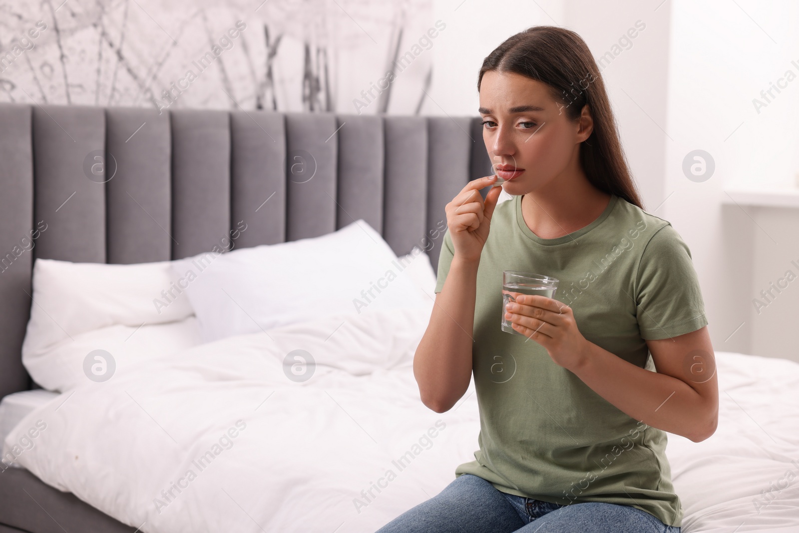 Photo of Depressed woman with glass of water taking antidepressant pill on bed indoors, space for text