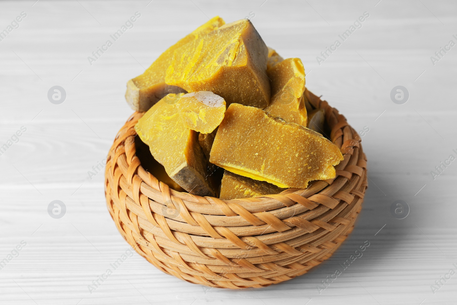 Photo of Wicker basket with natural organic beeswax blocks on white wooden table