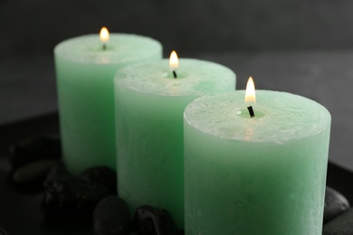 Photo of Three color burning candles and rocks on dark plate