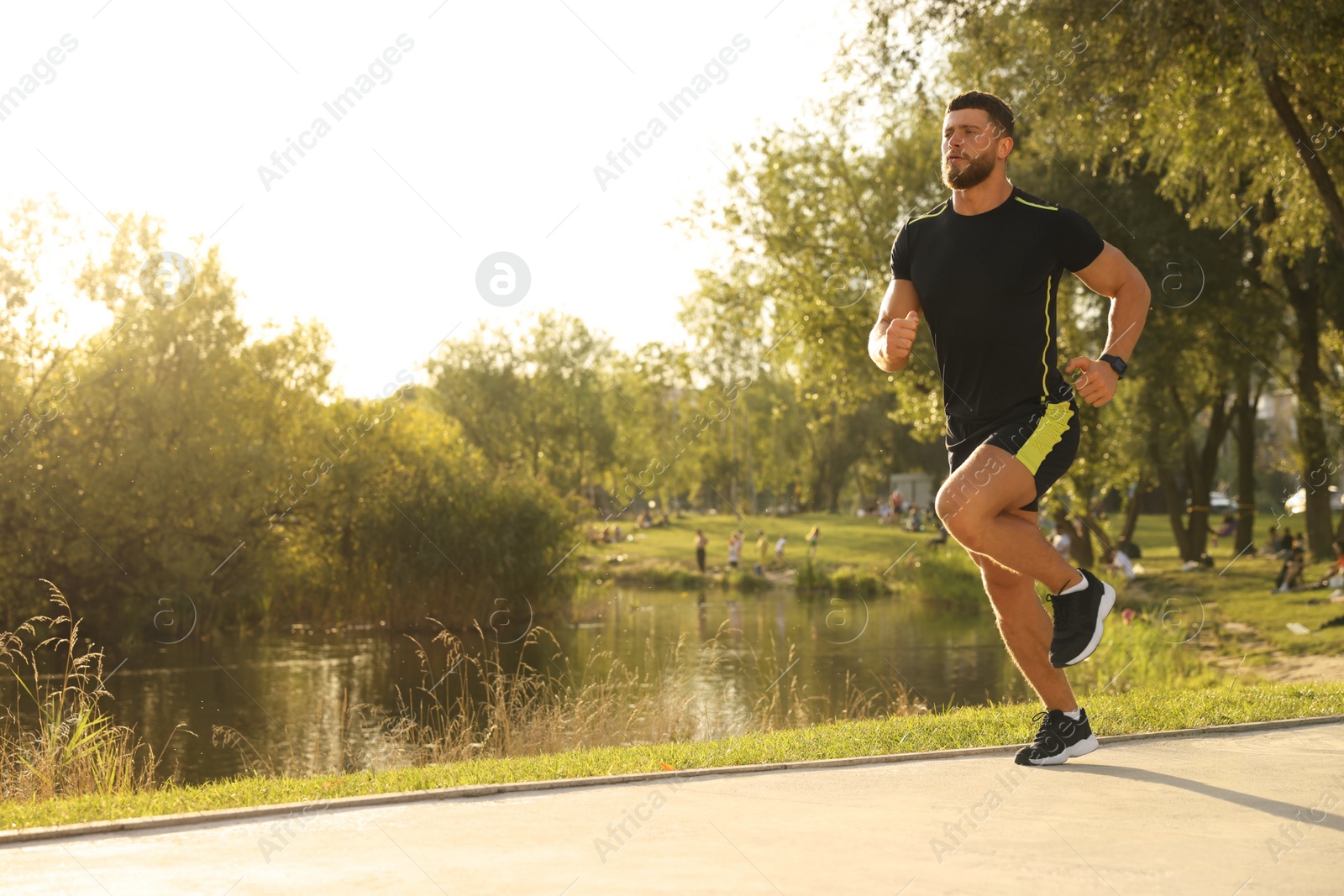 Photo of Young man running near pond in park. Space for text