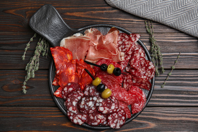 Photo of Tasty prosciutto and other delicacies served on wooden table, flat lay