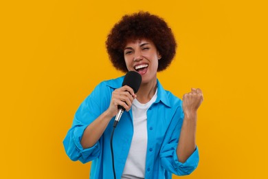 Curly young woman with microphone singing on yellow background