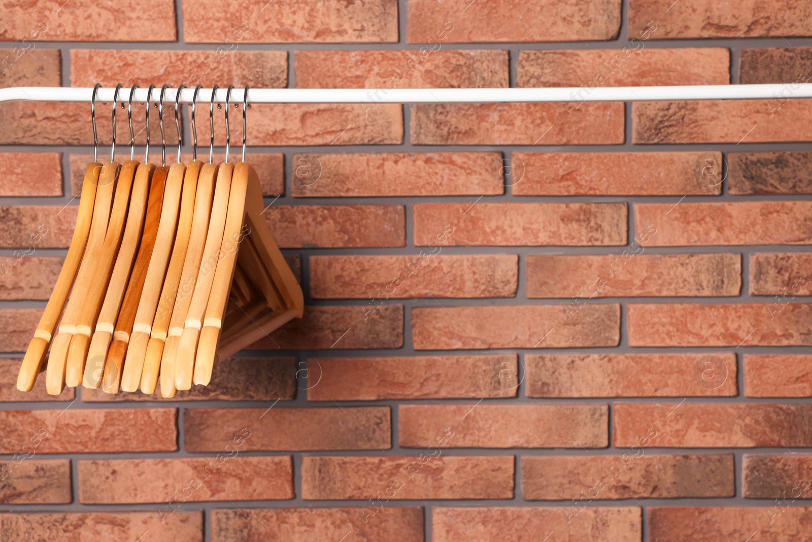 Photo of Wooden clothes hangers on rail near red brick wall. Space for text