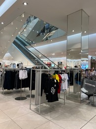 Racks with stylish clothes and escalator in shopping mall